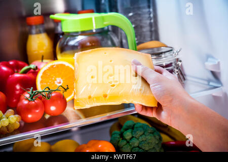 Frau nimmt das Stück Käse aus dem offenen Kühlschrank Stockfoto