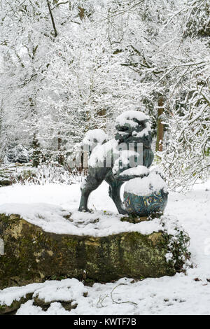 Chinese Foo Dog Bronzestatue und Winter Bäume im Schnee im Dezember bei Batsford Arboretum, Cotswolds, Moreton-in-Marsh, Gloucestershire, England Stockfoto