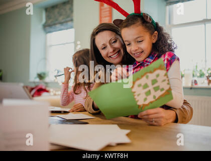 Kleine Mädchen und Schreiben von Weihnachtskarten mit ihrer Mutter am Esstisch in Ihrem Haus. Stockfoto