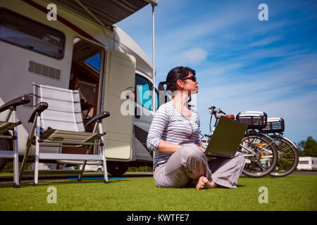 Frau, die auf dem Rasen, auf dem Laptop in der Nähe des Campingplatzes. Wohnwagen Auto Urlaub. Urlaub mit der Familie reisen, Urlaub im Wohnmobil Stockfoto