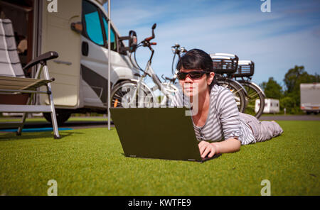 Frau, die auf dem Rasen, auf dem Laptop in der Nähe des Campingplatzes. Wohnwagen Auto Urlaub. Urlaub mit der Familie reisen, Urlaub im Wohnmobil Stockfoto