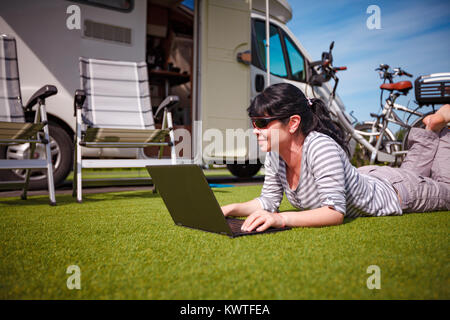 Frau, die auf dem Rasen, auf dem Laptop in der Nähe des Campingplatzes. Wohnwagen Auto Urlaub. Urlaub mit der Familie reisen, Urlaub im Wohnmobil Stockfoto