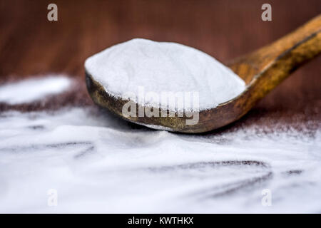 Natron oder Natriumhydrogencarbonat in eine hölzerne Schaufel auf den braunen Holz- Oberfläche. Stockfoto
