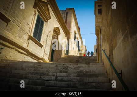 Typische Mittelalterliche Straße in Valetta, Malta, der Europäischen Kulturhauptstadt 2018, mit Treppen und Touristen die seitlichen Straßen genießen. Stockfoto