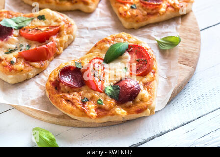 In Herzform mini Pizzen über Holz- Hintergrund mit kopieren. Mini Pizza mit Tomaten, Peperoni, Mozzarella und Basilikum für den Valentinstag Stockfoto