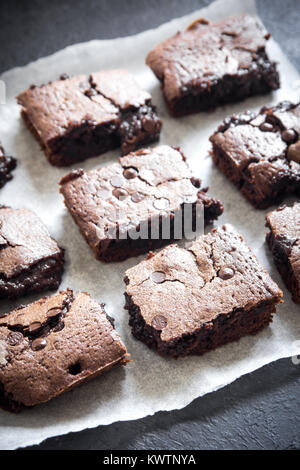 Double Chocolate Brownies. Hausgemachte Schokolade Fudge Brownies mit Chocolate Chips auf Backpapier und schwarzen Hintergrund. Stockfoto