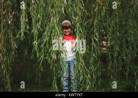 Wenig glücklich Mädchen versteckt sich in der Willow Laub Stockfoto