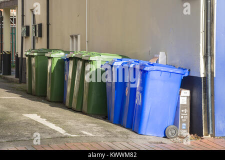 Zeile mit blauen und grünen Wheelie bins außerhalb einer weiß getünchten Gebäude Stockfoto