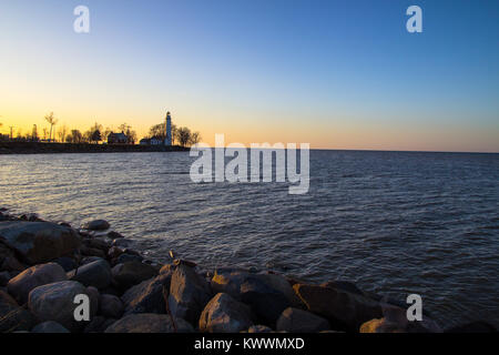 Leuchtturm in der Ferne Ufer. Leuchtturm auf dem entfernten Ufer des Lake Huron bei Sonnenaufgang. Point Aux Barques Leuchtturm, Port Hope, Michigan, USA. Stockfoto