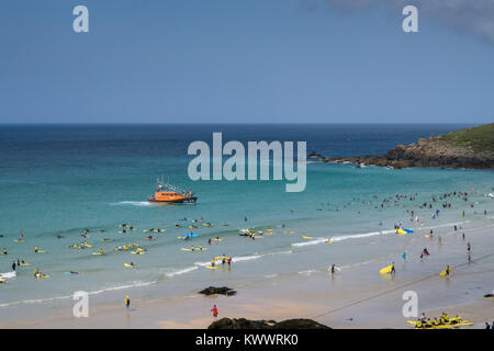 Ein Sommertag am Strand St Ives in Cornwall. Die RNLI lifeboat Patrouillen offshore während Surfers und Touristen die schönen sonnigen Bedingungen genießt. Stockfoto