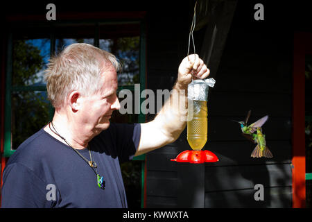 Mann hält eine Kolibrizufuhr bei Los Quetzales in La Amistad National Park Lodge, Provinz Chiriqui, Republik Panama. Stockfoto