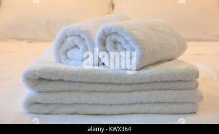 Hotel Schlafzimmer. White rollte und gefalteten Handtücher, weiße Bettwäsche Kulisse. Nahaufnahme, Details. Stockfoto