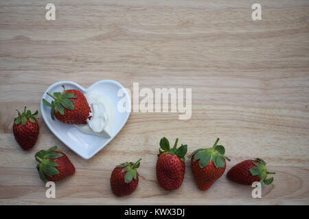 Essen Fotografie Bild mit gesunde Frucht saftige rote Erdbeeren und Sahne in einem weißen Liebe Herzform Schüssel auf hellem Hintergrund mit Platz Stockfoto