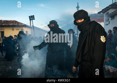 Antigua, Guatemala - 19. April 2014: Mann in schwarzen Roben und Hauben Räucherwerk verbreiten sich in einer Strasse der Stadt Antigua während einer Prozession der Stockfoto