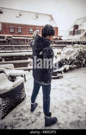 Ein Junge, kid Schneebälle in einem Hinterhof ist, geniessen die ersten Schnee im späten Herbst. Stockfoto