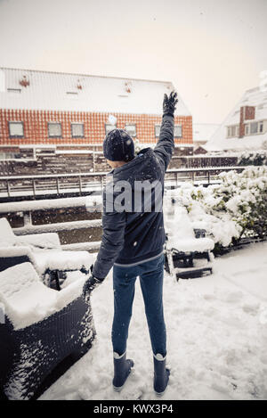 Wenig junge wirft Schneebälle in einem Hinterhof, genießen den ersten Schnee im späten Herbst. Stockfoto