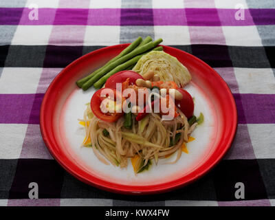 Thai Green Papaya Salat, Som Tam, berühmte Straße essen von Thailand in traditionellen Blumendruck Fach auf lila Thailändischen lendenschurz Hintergrund Stockfoto