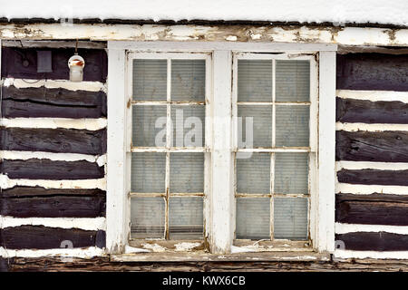 Das Fenster in der Seite einer Blockhütte mit zwischen den Protokollen verpackt das Stopfen. Stockfoto