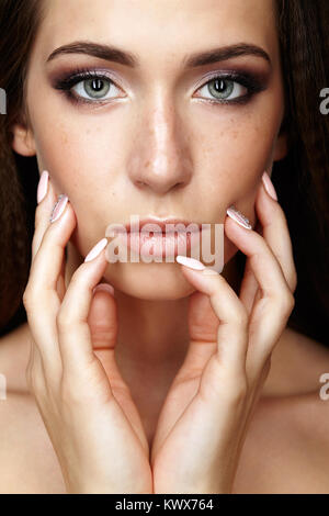 Schönheit Porträt der jungen Frau Gesicht mit den Fingern zu berühren. Brunette Mädchen mit langen Haaren und Tag weibliche Make-up. Stockfoto