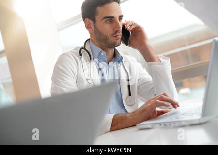 Junger Arzt im Büro Arbeiten am Laptop und am Telefon sprechen Stockfoto