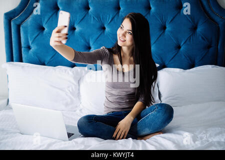 Glückliche Frau auf dem Bett liegend und Selfie Foto auf Smartphone zu Hause Stockfoto