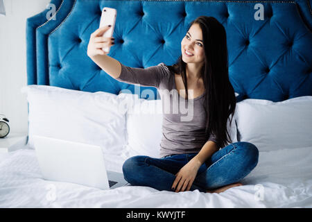 Glückliche Frau auf dem Bett liegend und Selfie Foto auf Smartphone zu Hause Stockfoto
