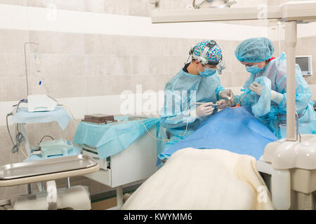 Zahnarzt Team arbeiten mit Patienten. Zahnärztliche Chirurgie. Zahnarzt in Maske mit Lupe Fernglas Stockfoto