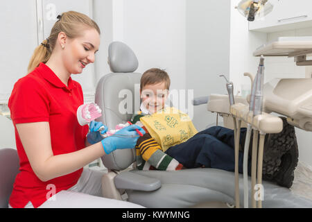 Der Zahnarzt, der kleine Junge wie die Zähne mit einer Zahnbürste auf einen künstlichen Kiefer dummy reinigen. Madical Büro Stockfoto