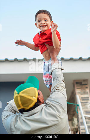 Happy Hispanic junge in der Luft mit seinem Vater palying Stockfoto