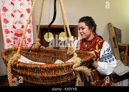 Frau, die in der ukrainischen native Kleid rockt ein traditionelles Gestell mit einem Baby. Januar 4,2018. Kiew, Ukraine Stockfoto