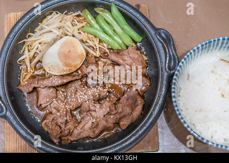 Koreanische gegrilltes Schweinefleisch in heißer Pfanne mit Ei, sprießen und Erbsen auf Seite. Stockfoto