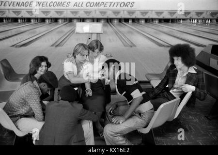 Schwarze britische Jungen und weiße Mädchen, eine Gruppe von Teenagern, die in der Bowlingbahn Stevenage Hertfordshire herumhängen und Zigaretten rauchen. 70er Jahre England 1975 Großbritannien HOMER SYKES Stockfoto