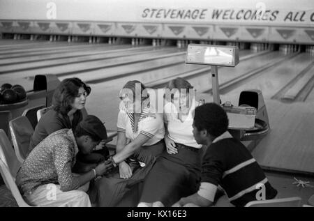 Schwarze britische Jungen und weiße Mädchen, eine Gruppe Teenager, die in der Bowlingbahn Stevenage Hertfordshire 1970er England 1975 UK HOMER SYKES rumhängen Stockfoto