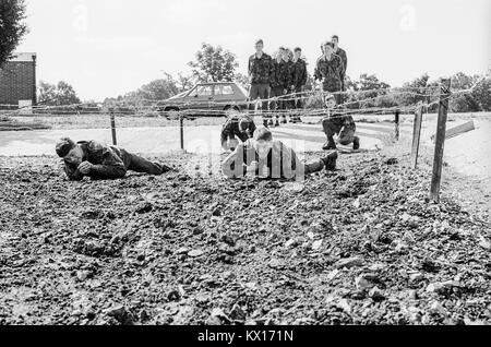 Britische Armee squaddies in der Ausbildung durch Schlamm kriechen unter Stacheldraht als Teil eines Hindernisparcours. England. 15. Juni 1993 Stockfoto