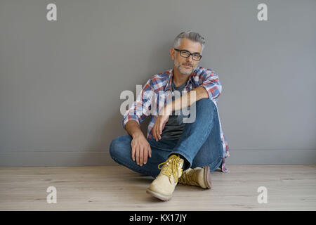 Trendy 40-Jahre alte Mann sitzt auf dem Boden, isoliert Stockfoto