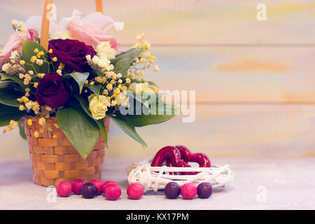 Romantische Stillleben mit einem Korb von duftenden Rosen, Rattan Kranz mit roten Herzen innerhalb und farbigen runde Bonbons auf dem Tisch. Helle Holz- backgrou Stockfoto