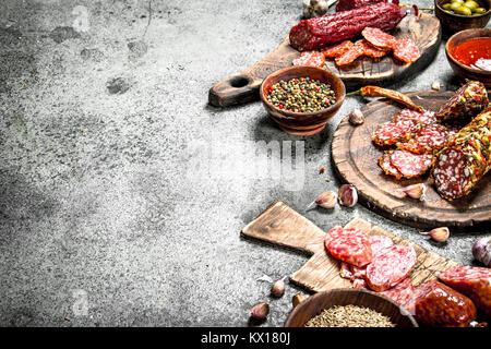 Verschiedene Arten von Salami mit Gewürzen und Kräutern auf alten Karten. Auf einem urigen Hintergrund. Stockfoto