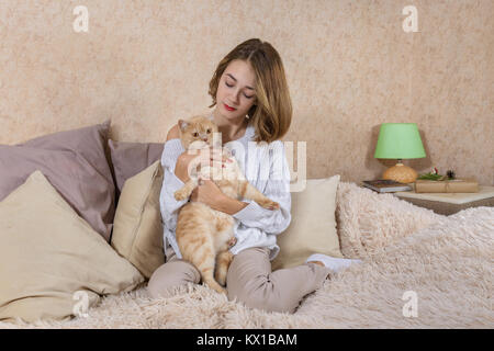 Das Mädchen im weißen Pullover sitzen auf der Couch und umarmen eine rote Katze Stockfoto