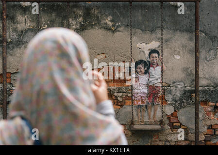 Eine Mutter nimmt ein Foto von ihrem Sohn auf einem Stück interaktive Street Art von Ernest Zacharevic in Georgetown, Penang, Malaysia sitzen. Stockfoto