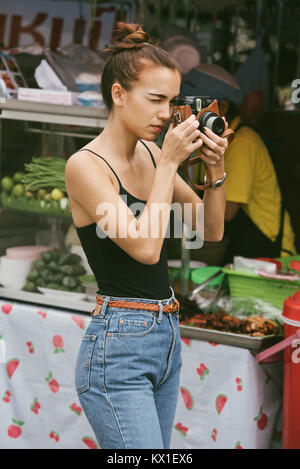 Eurasischen (halb europäisch, halb Asiatisch) Mädchen nimmt ein Foto auf den Straßen von Bangkok, Thailand mit einer Polaroid Kamera. Stockfoto
