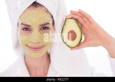 MODEL RELEASED. Junge Frau mit eine halbe Avocado tragen Gesichtsmaske, Studio gedreht. Stockfoto