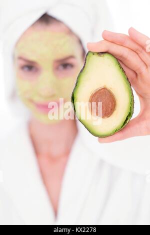 MODEL RELEASED. Junge Frau mit eine halbe Avocado tragen Gesichtsmaske, Studio gedreht. Stockfoto