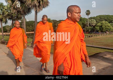 Drei buddhistischen Mönchen in den traditionellen Safran Seide Gewänder gekleidet zu Fuß den Sandstein Straße in die Tempel Angkor Wat, Siem Reap, Kambodscha. Stockfoto