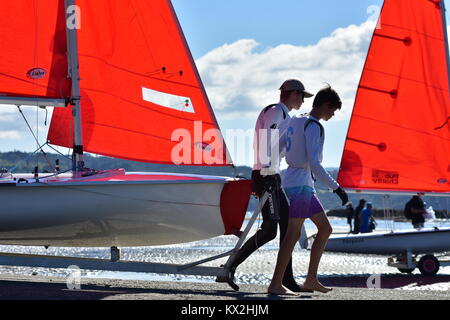 Crew abschleppen racing Jolle mit rotem Segel am Sandstrand. Stockfoto