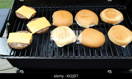 Hamburger Pastetchen mit verarbeitetem Käse kochen auf einem Tisch im Freien top Grill. Brötchen Schiebeschalter neben Stockfoto