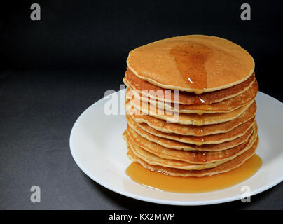 Stapel von Frische, hausgemachte Pfannkuchen mit Ahornsirup, serviert auf weiße Platte, schwarzer Hintergrund Stockfoto