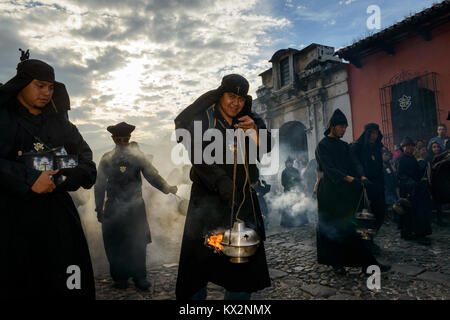 Antigua, Guatemala - 19. April 2014: Mann in schwarzen Roben und Hauben Räucherwerk verbreiten sich in einer Strasse der Stadt Antigua während einer Prozession der Stockfoto