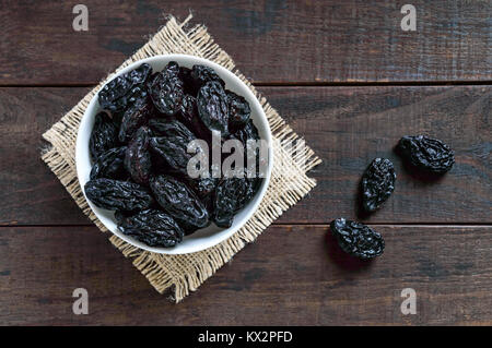 Pflaumen in einer Keramikschale auf einem dunklen Hintergrund. Getrocknete Früchte. Die Ansicht von oben Stockfoto