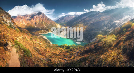 Blick auf die hohen Berge des Himalaja, erstaunliche Berg See mit türkisfarbenem Wasser, Hügel, gelben Gras, Bäume und blauer Himmel mit Wolken bei Sonnenuntergang in Stockfoto