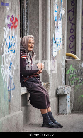 Lokale Lebensstil: armen alten Frau sitzt auf einem Fenstersims mit Graffiti betteln von Passanten in Bukarest, der Hauptstadt Rumäniens, Mitteleuropa Stockfoto